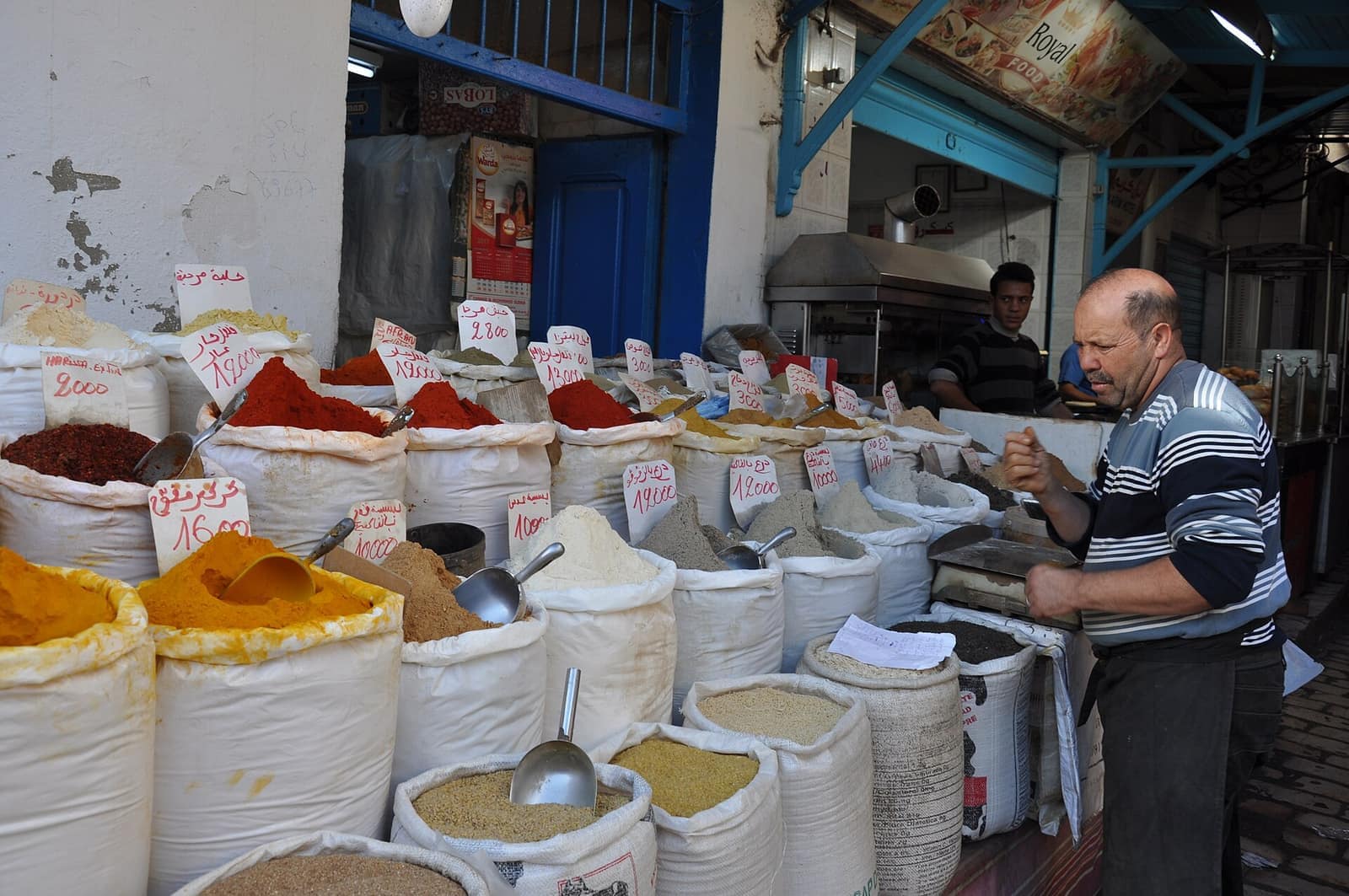 Épicier du souk derrière ses sacs d'épices : harissa, curcuma, couscous