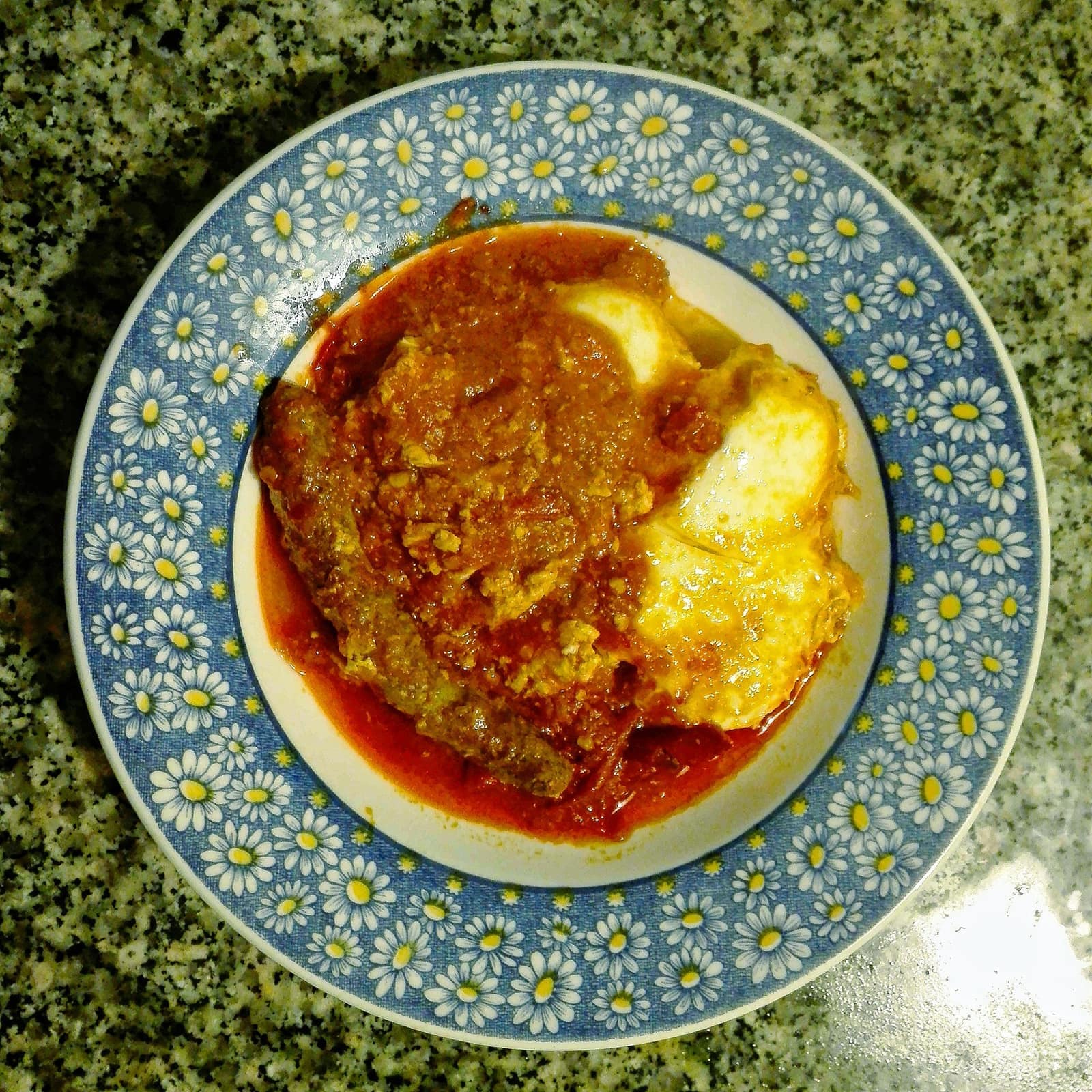 Ojja aux merguez et œufs coulants dans une assiette en faïence bleue