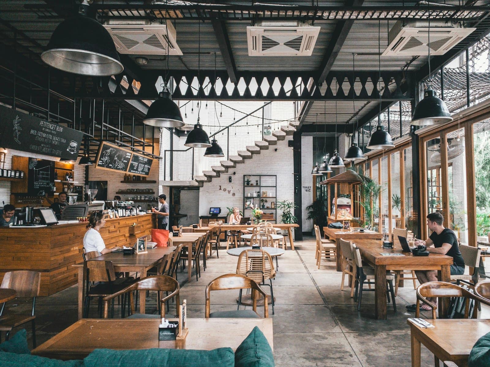 Salle du restaurant baignée de lumière, tables en bois et verrière